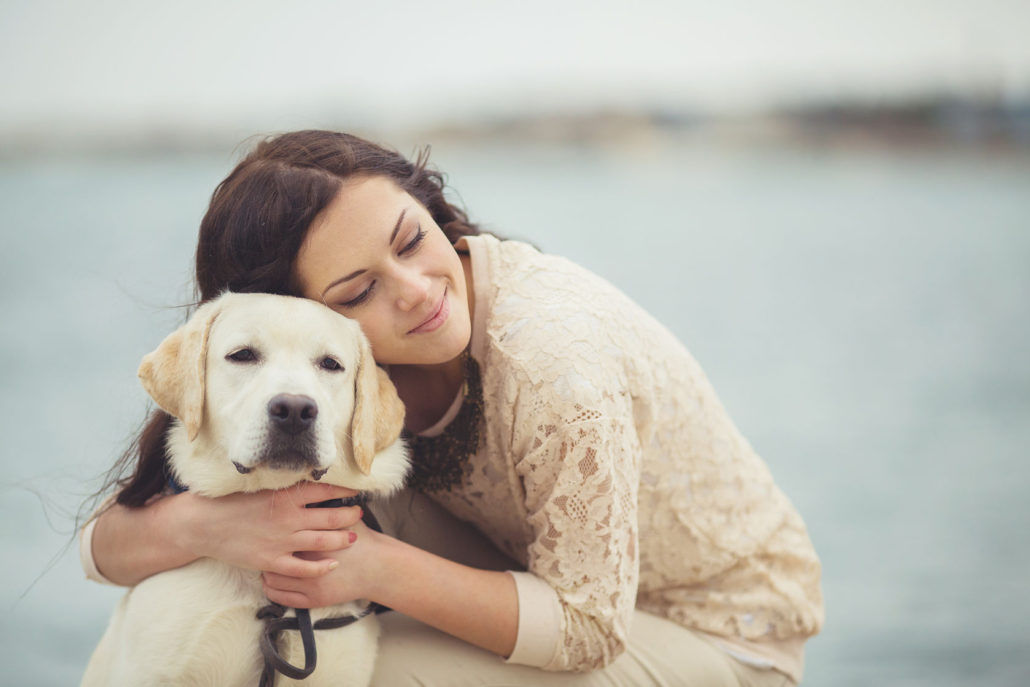 portrait of beautiful young woman playing with dog on the sea shore